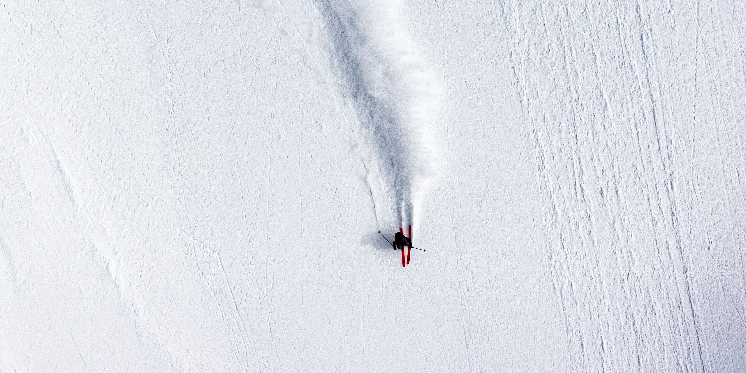 Luftaufnahme einer Powder-Abfahrt: Freerider zieht eine Schneefahne durch unverspurten Tiefschnee
